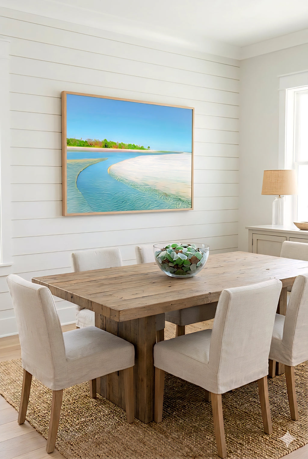Coastal beach wall art in neutral dining room with rustic wood table, upholstered chairs, white shiplap walls, and turquoise shoreline print for relaxed coastal decor styling