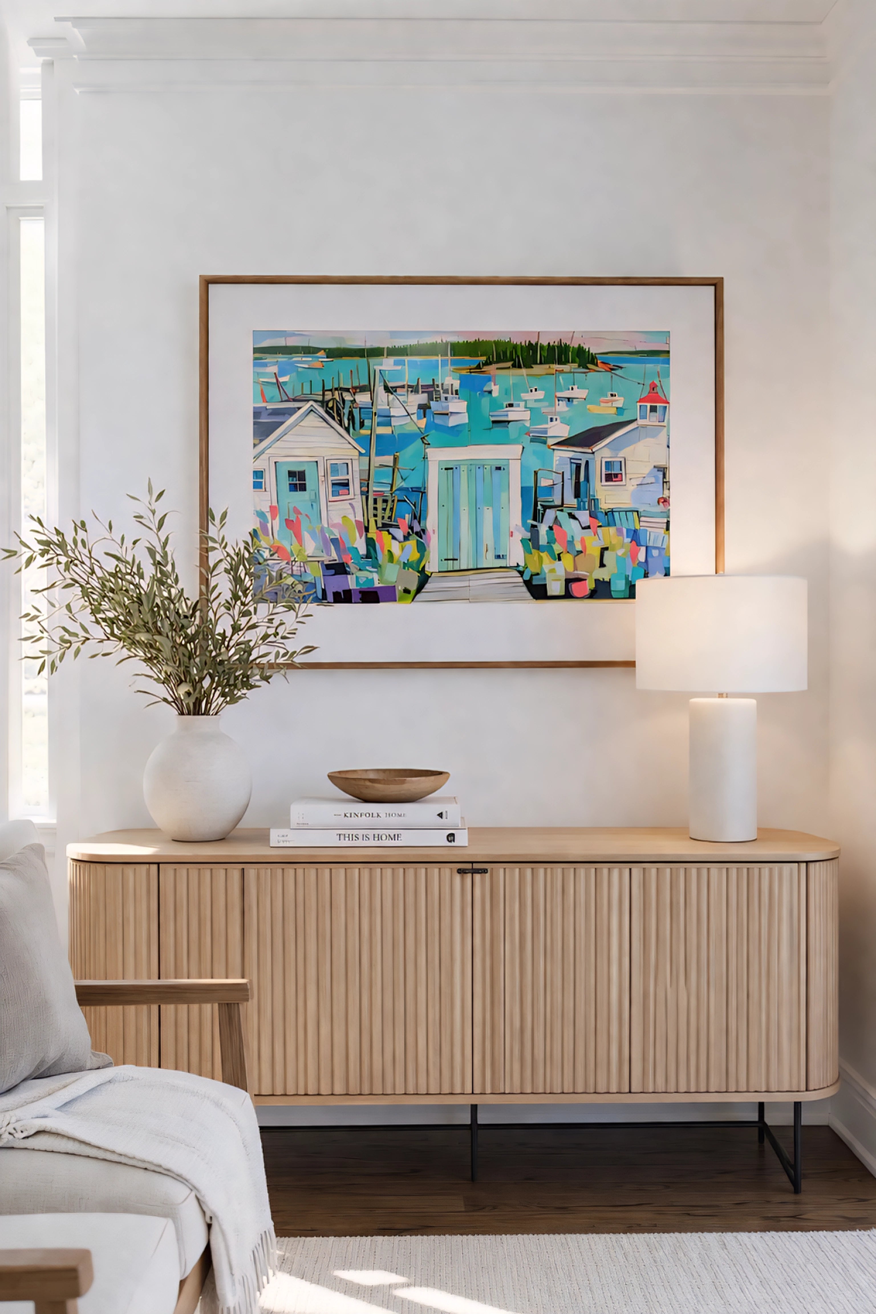 Coastal harbor wall art printable above wood sideboard in neutral living room with soft decor and lamp, colorful nautical boats painting horizontal beach house decor