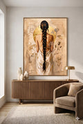 Large neutral boho wall art featuring a woman with a long braid and gold accents displayed above a modern wood console table with warm minimalist decor and soft beige tones